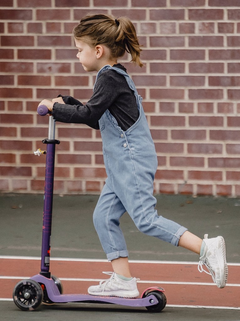 Photo of a child riding on a two-wheeled scooter with handlebars, by Allan Mas: https://www.pexels.com/photo/little-girl-riding-scooter-on-stadium-5622330/